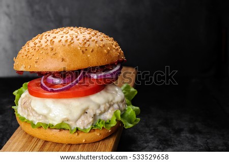 Fresh homemade burger with chicken burger cutlet, tomato sauce and mozzarella cheese in traditional buns, served on wood chopping board over dark background