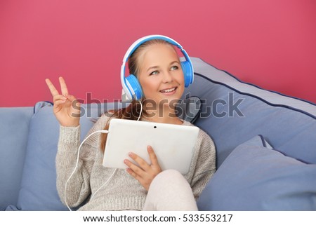 Cute teenager with tablet sitting on sofa in room