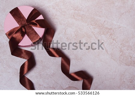 Round gift box with brown ribbons on a marble background. Space for text