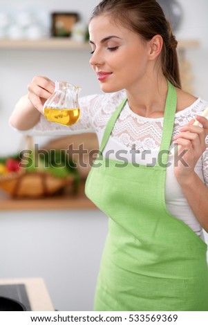 Young woman in the green apron cooking in the kitchen. Housewife smelling the oil while enjoys prepairing salad