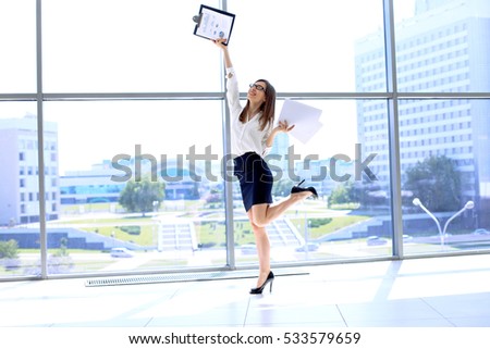 Happy modern business woman with financial report is running in office hall  