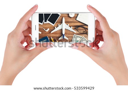 Woman hand using smart phone searching Preparation traveling with pencil, money, passport, airplane, watch, noted book, eyeglasses, earphone and photo frame on vintage wooden. Travel concepts.