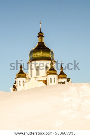 Beautiful Orthodox Church, winter view, play of sunlight on the gilded dome, blue sky in the background, white snowdrift with trodden traces in the front.