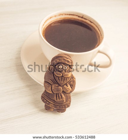 Cup of coffee and chocolate Christmas figurine on white wooden background