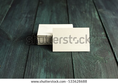 A photo of a blank white thick cardboard business card next to a pile of them, on a dark wooden background texture. A mockup or a minimalist banner with copyspace