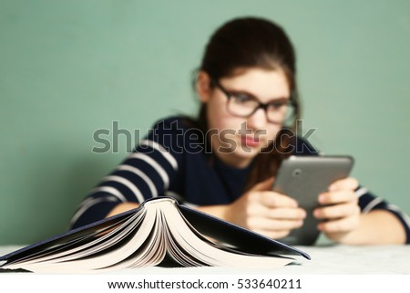 teenager girl in myopia glasses play online game on tablet refuse to read book.