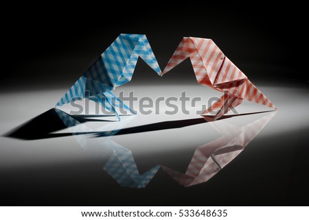 Red and blue origami birds made from striped paper isolated over black background