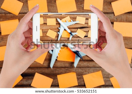 Woman hand using smart phone taking photo for preparation traveling and to do list with paper noted and airplane on vintage wooden background. Travel concepts, blurry background.