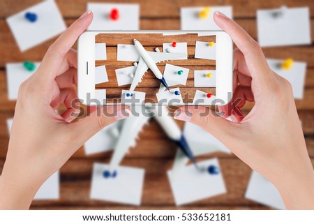 Woman hand using smart phone taking photo for preparation traveling and to do list with paper noted, airplane and colorful push pin on vintage wooden background. Travel concepts, blurry background.