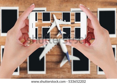 Woman hand using smart phone taking photo for preparation traveling with airplane and photo frame on vintage wooden background. Travel concepts, blurry background.