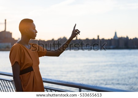 Young fashionable african woman pointing finger at Manhattan, New York skyline view as virtual reality