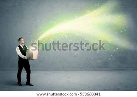 Bright yellow, green light beams escaping a cardboard box held by young elegant male business person in stylish suit concept.