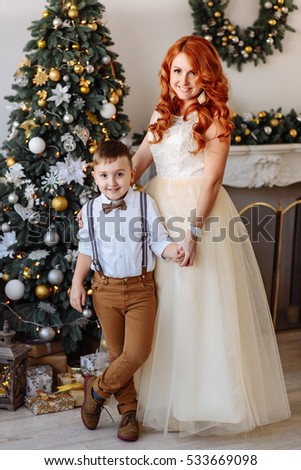 Mother and son standing near a Christmas tree in a white room with Christmas decorations