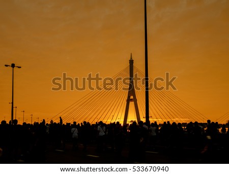 Silhouette of elevated expressway and crowd of people cross the river at twilight. Movement.