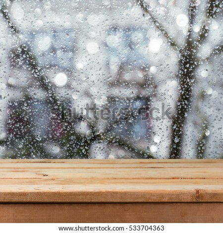 Empty wooden deck table over wet glass window. Rainy weather concept. Background for product montage display