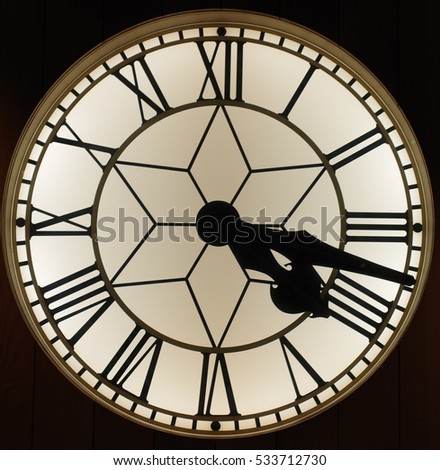 A close up of a circular clock with roman numerals. The time is twenty past four. It has a black background.  The inside of the clock has a star shape. Royalty-Free Stock Photo #533712730