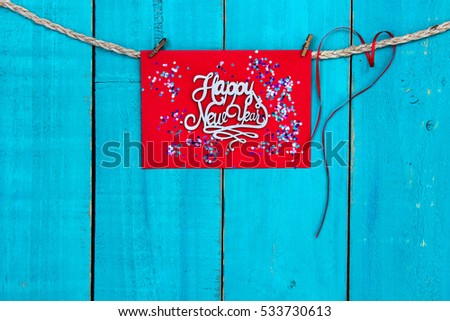 Colorful Happy New Year sign hanging from rope with holiday confetti and red ribbon heart on blank antique rustic teal blue textured wood background; color copy space for text 