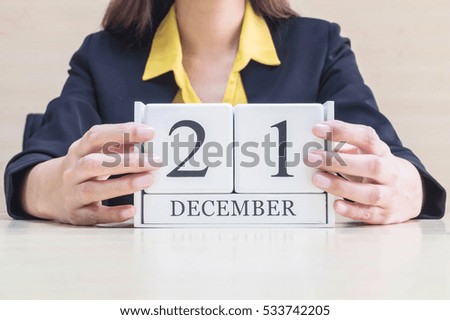 Closeup white wooden calendar with black 21 december word in blurred working woman hand on wood desk in office room , selective focus at the calendar