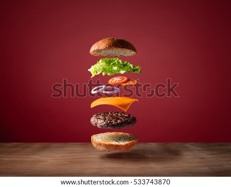 Delicious burger with floating ingredients on the wood table red background