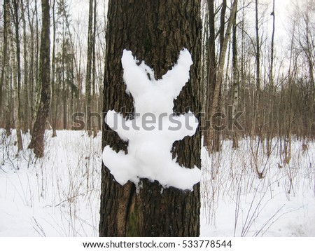 Figure of bunny animal made of snow on the tree at the winter landscape. Family fun at the city park scene. Funny picture with forest background.