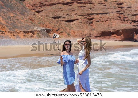 Two young  women making selfie on the beach with rocks background.