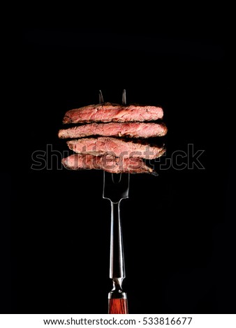 Slices of Medium rare grilled Steak Ribeye on meat fork on black background Royalty-Free Stock Photo #533816677