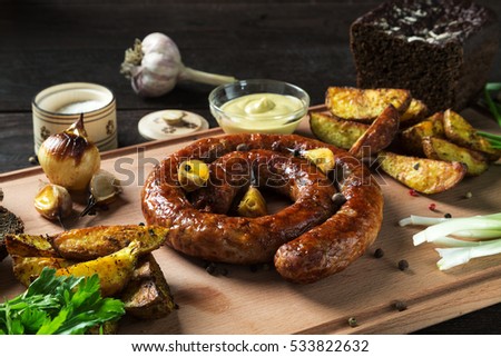 Fried sausage on a rustic wooden table, with herbs and spices, wood background. Served on a wooden board with mustard, bread, onion, garlic and baked potatoes. Horizontal image.