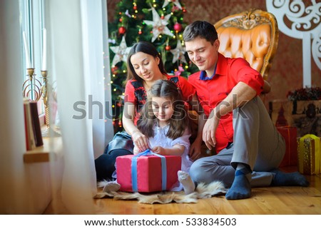 happy family opens gifts, sitting on a floor near a window. On a background the Christmas tree. Waiting for the Holiday.