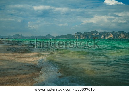 Sandy beach in tropical island with green ocean water and mountain silhouette background