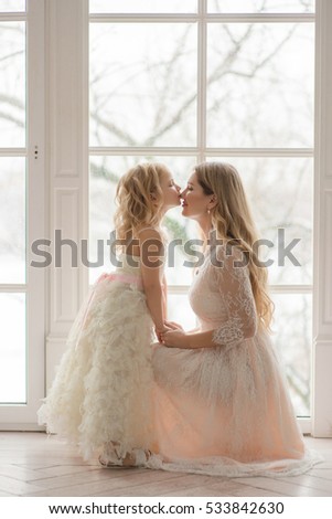 beautiful blonde mother and daughter kissing in front of the window