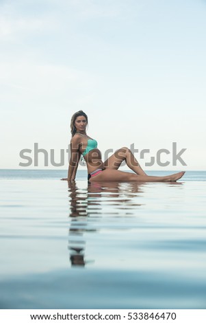 a beautiful Woman in an infinity pool side view of the beautiful shapes of young women, beautiful hotel in the background, a summer resort the sea and horizon