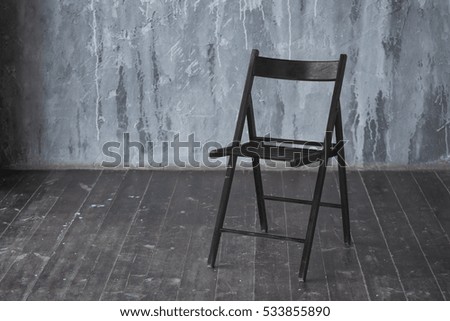 Black wooden chair standing in front of a grey urban wall with mouldings on wooden black floor.