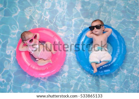 Two month old twin baby sister and brother sleeping on tiny, inflatable, pink and blue swim rings. They are wearing crocheted swimsuits and sunglasses. Royalty-Free Stock Photo #533865133