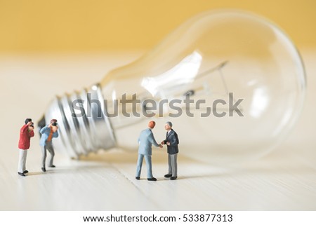 business miniature people make handshaking agreement with light bulb background