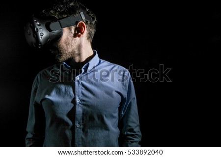 young bearded man using VR virtual reality glasses headset. art light photo. dark grey background