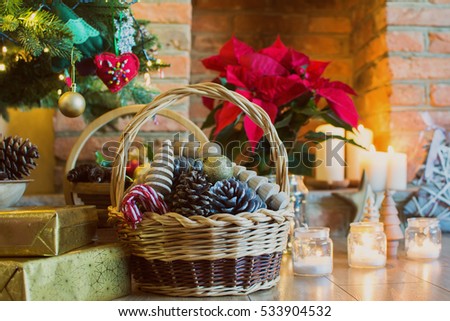 Christmas setting background: decorated Christmas tree, pine cones in the basket, wooden trees, poinsettia with fireplace on the background; candles and lights, selective focus. Toned photo