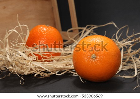 Two mandarin on a black background. Two tangerine with a box with hay. Space for text