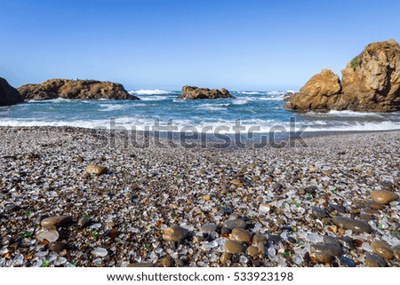 Beautiful sea glass in a variety of colors with blue waves and sky in Fort Bragg, California