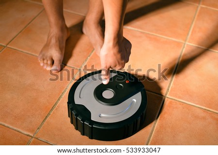 Human hand using smart robotic technology vacuum cleaner cleaning floor tiles background. Closeup top view image
