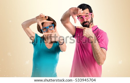 Couple in colorful clothes focusing with their fingers on ocher background