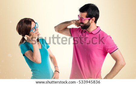 Couple in colorful clothes making phone gesture on ocher background