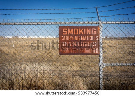 Smoking, Carrying Matches, Open Lights, Positively Prohibited - Rusty Metal Sign with Chain Link Fence - Casper Wyoming.
