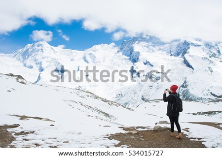 young woman taking a picture of snow mountains with smartphone, switzerland