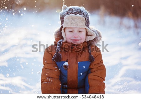 Happy child boy playing on a winter walk in nature during snowfall.