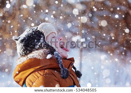 Portrait of a cute little boy in warm clothes who catches snowflakes mouth in winter sunny day