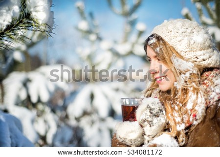 Girl with a cup of tea in the winter forest. Young woman enjoying nature, snow and sunny mood.