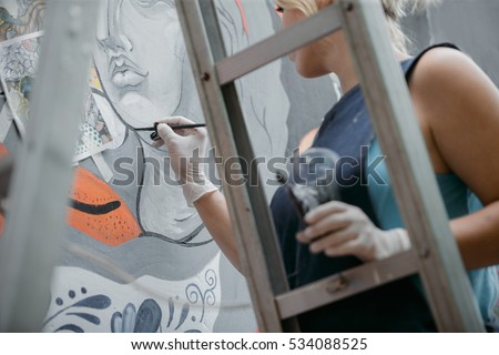  Cheerful young woman painting on the wall. 
