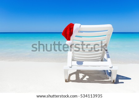 Santa Claus Hat on sunbed near tropical calm beach with turquoise caribbean sea water and white sand. Christmas vacation celebration Royalty-Free Stock Photo #534113935
