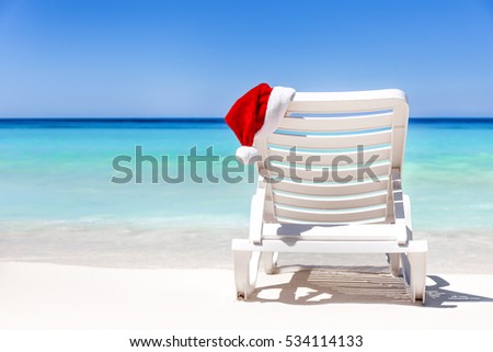 Santa Claus Hat on sunbed near tropical calm beach with turquoise caribbean sea water and white sand. Christmas vacation concept Royalty-Free Stock Photo #534114133