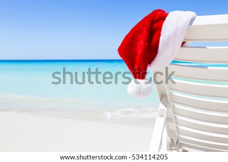 Santa Claus Hat on sunbed near tropical calm beach with turquoise caribbean sea water and white sand. Christmas vacation celebration Royalty-Free Stock Photo #534114205